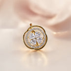 A gold flower-shaped pendant with a five-petal floral center and a surrounding double-ring halo of small clear stones, shown on a soft beige satin background.