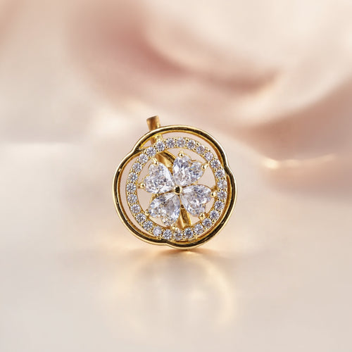 A gold flower-shaped pendant with a five-petal floral center and a surrounding double-ring halo of small clear stones, shown on a soft beige satin background.