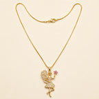Gold fairy pendant necklace with CZ crystals and pink flower charm, close-up product photo on beige background