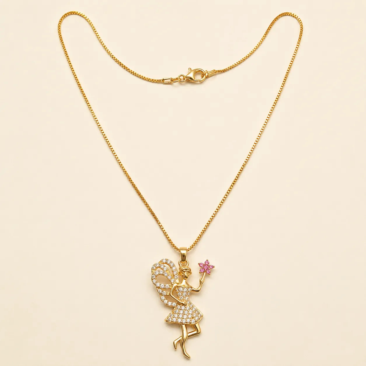 Gold fairy pendant necklace with CZ crystals and pink flower charm, close-up product photo on beige background