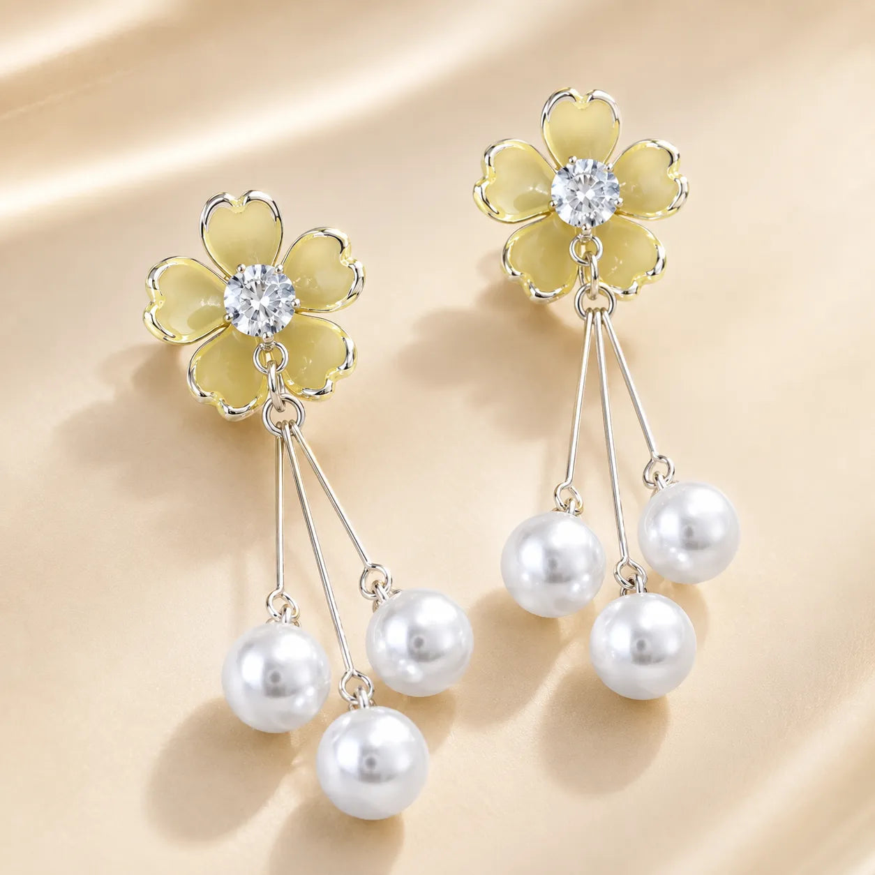 "Yellow enamel flower earrings with silver chain and pearl drops on silk fabric"