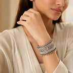 Woman wearing silver wide cuff bangle with white enamel checkerboard borders and ghungroo chain drops on wrist styled with cream silk outfit
