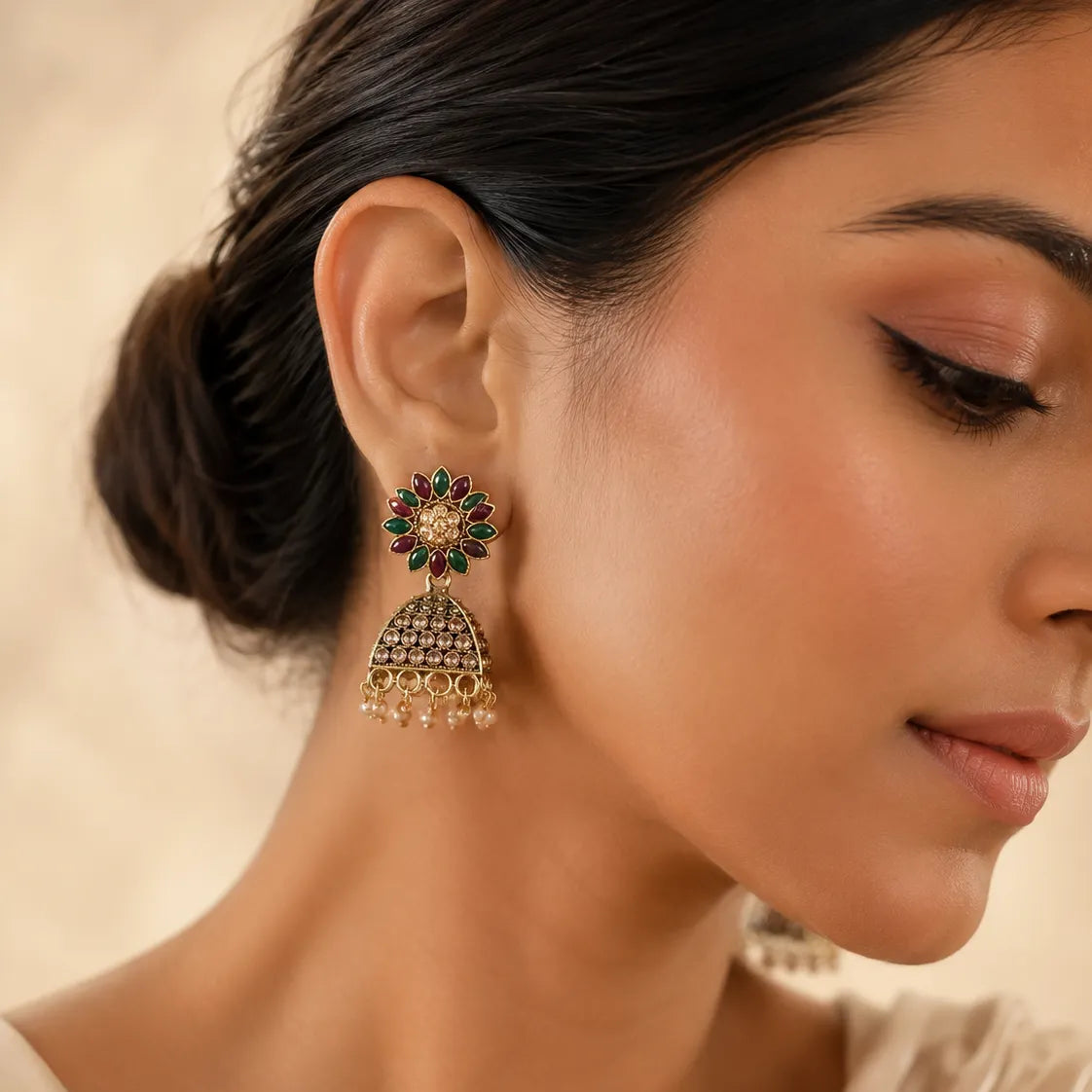 Woman wearing antique gold ruby emerald floral jhumka earrings with pearl drops and champagne crystal dome styled with cream silk saree