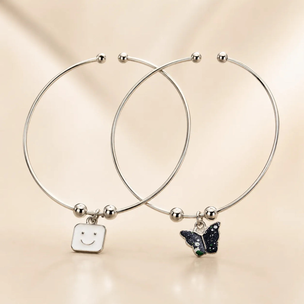 Silver smiley face and black butterfly enamel charm bangle bracelet set of 2 overlapping on beige background
