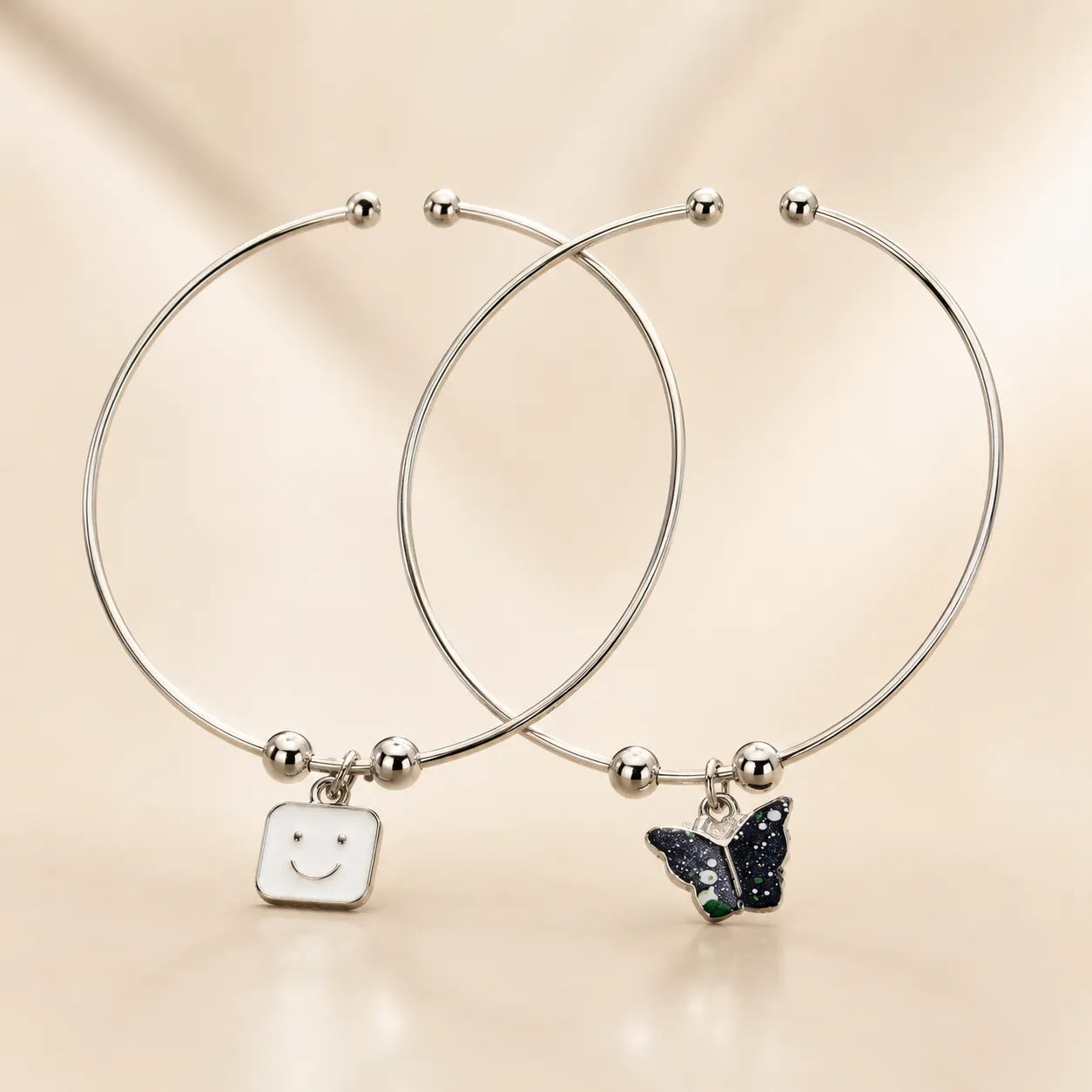 Silver smiley face and black butterfly enamel charm bangle bracelet set of 2 overlapping on beige background