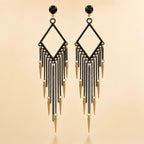 Black chandelier fringe earrings with gold spike charms, geometric diamond frame and black crystal stud, front view on beige background
