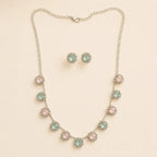 Pink and mint crystal halo necklace and earring set coiled on beige fabric, showing extendable chain and clasp detail