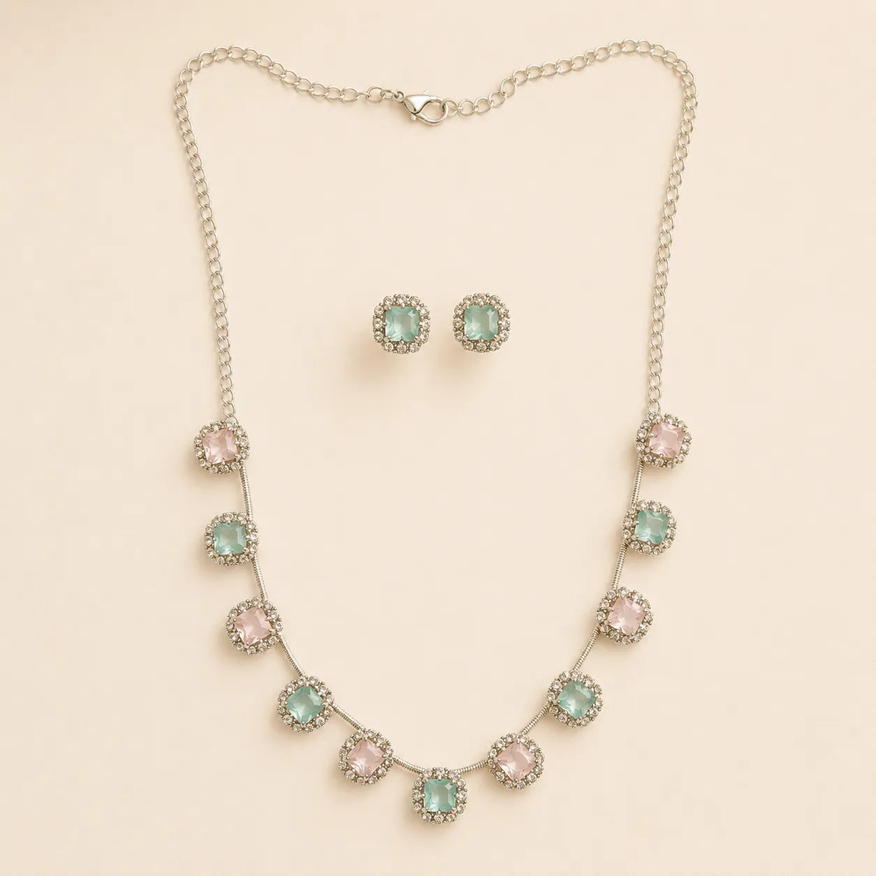 Pink and mint crystal halo necklace and earring set coiled on beige fabric, showing extendable chain and clasp detail