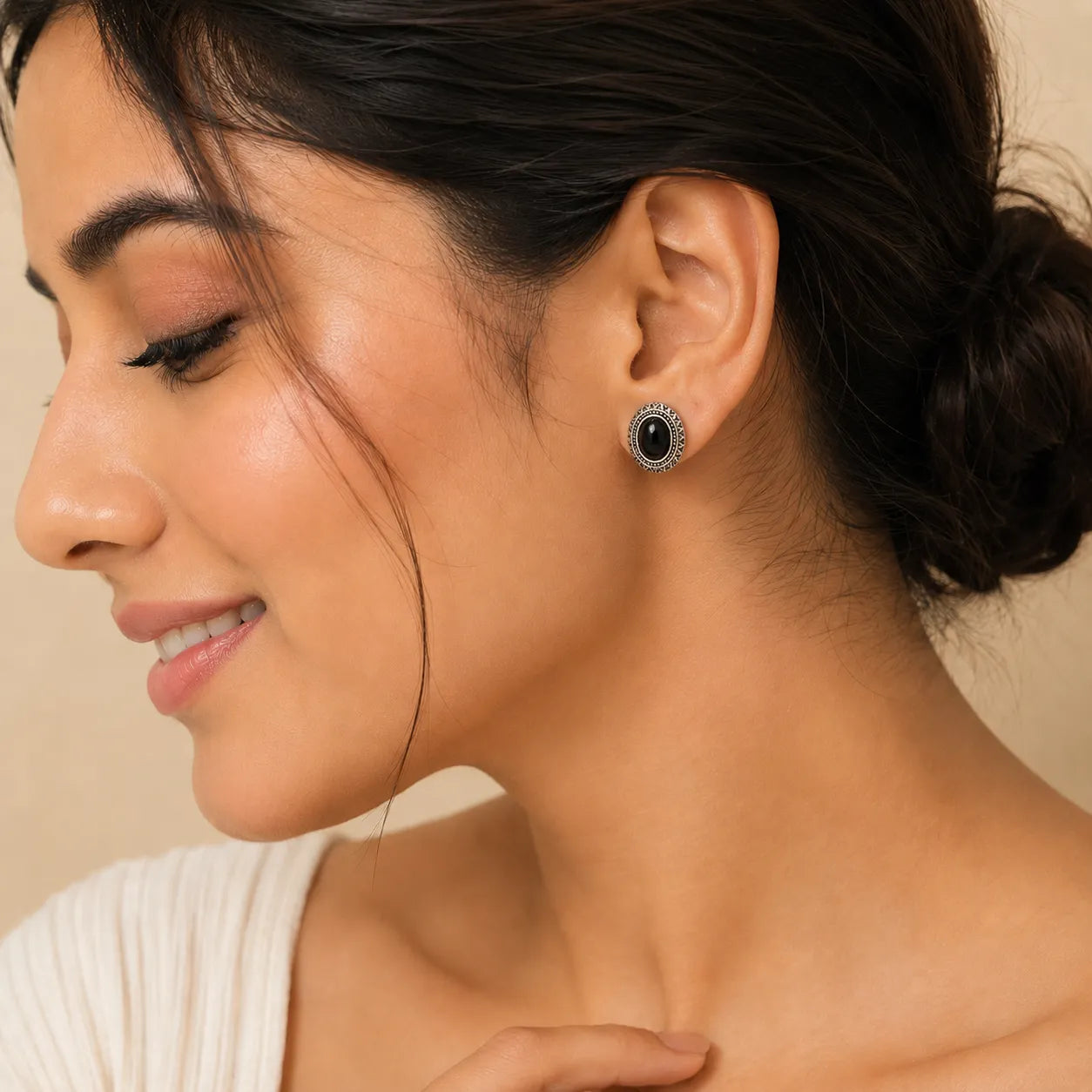 "Woman wearing oval black stone stud earring with silver aztec border"