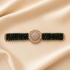 A jewelry set displayed on a cream-colored box, featuring a wide beaded bracelet with a large floral centerpiece and matching drop earrings, both in dark green and rose gold with clear rhinestone accents.