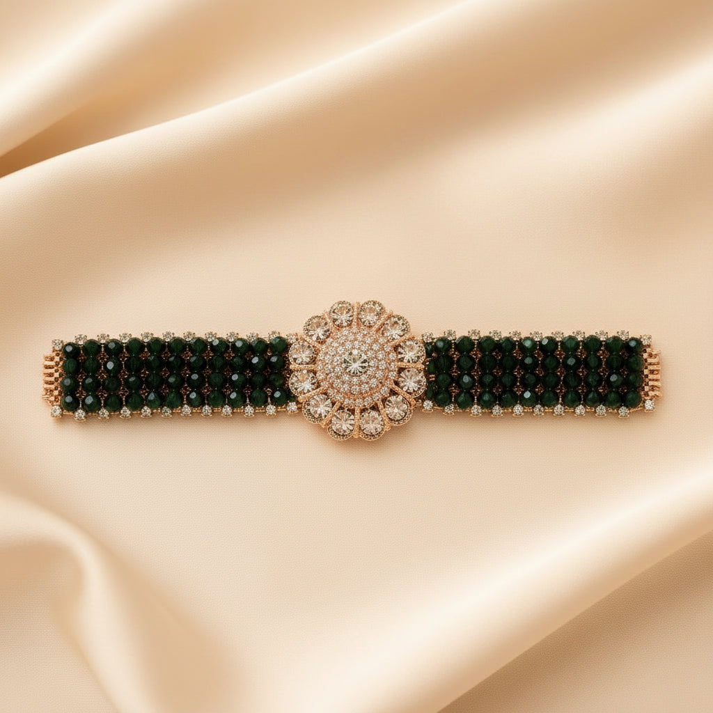 A jewelry set displayed on a cream-colored box, featuring a wide beaded bracelet with a large floral centerpiece and matching drop earrings, both in dark green and rose gold with clear rhinestone accents.