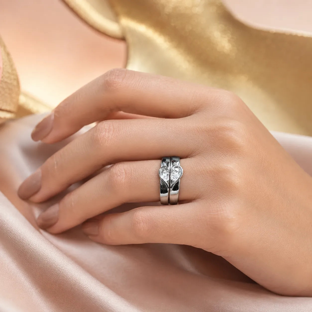 A close-up of a hand wearing a silver ring with a sculpted, textured band, resting on soft champagne-colored satin fabric.
