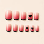 SAVNI pink ombre press-on nails with black French tips and heart accents, glossy fake nail set on beige background