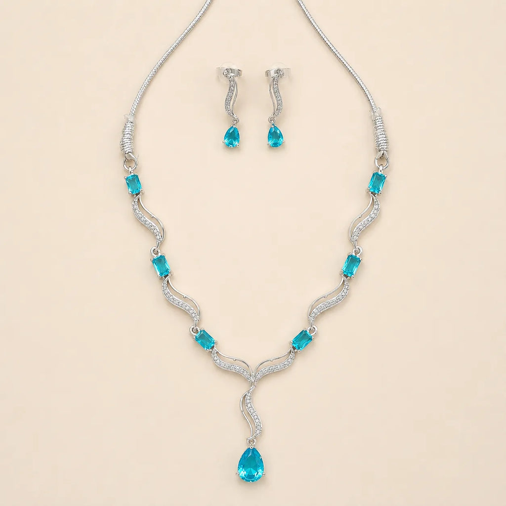 Angled view of silver blue crystal necklace and matching drop earrings on beige background