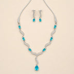 Angled view of silver blue crystal necklace and matching drop earrings on beige background