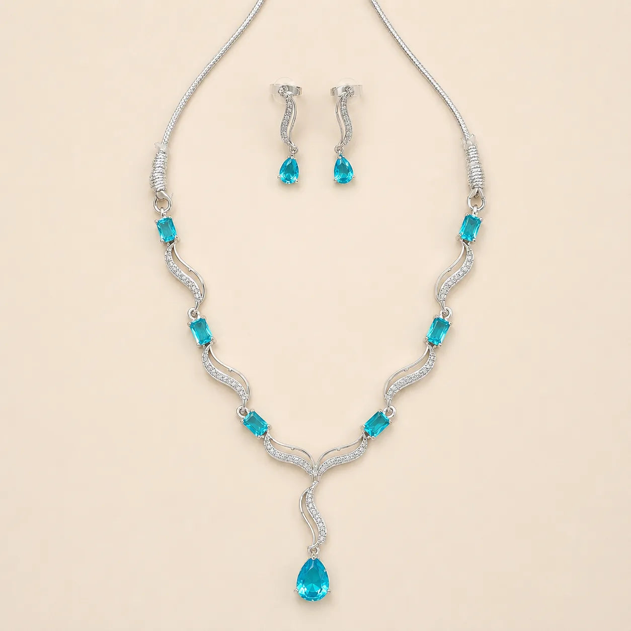 Angled view of silver blue crystal necklace and matching drop earrings on beige background