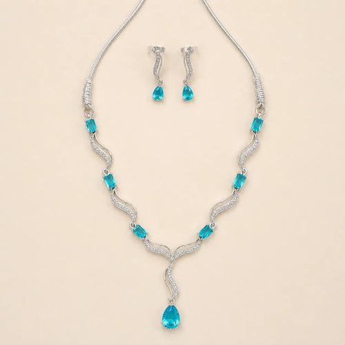 Angled view of silver blue crystal necklace and matching drop earrings on beige background