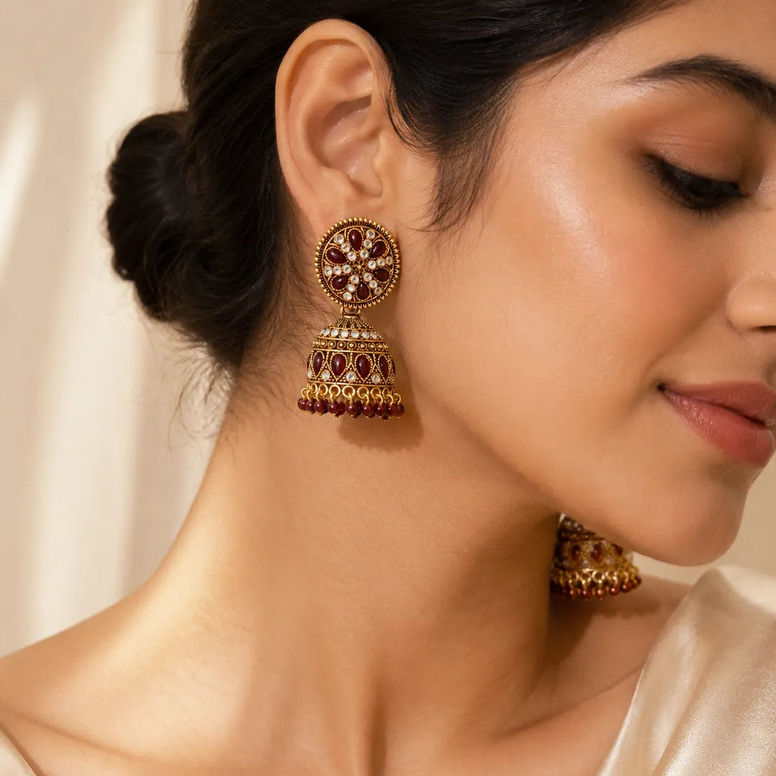 Bride wearing antique gold maroon kundan circular disc stud jhumka earrings with bead drops styled with cream satin saree