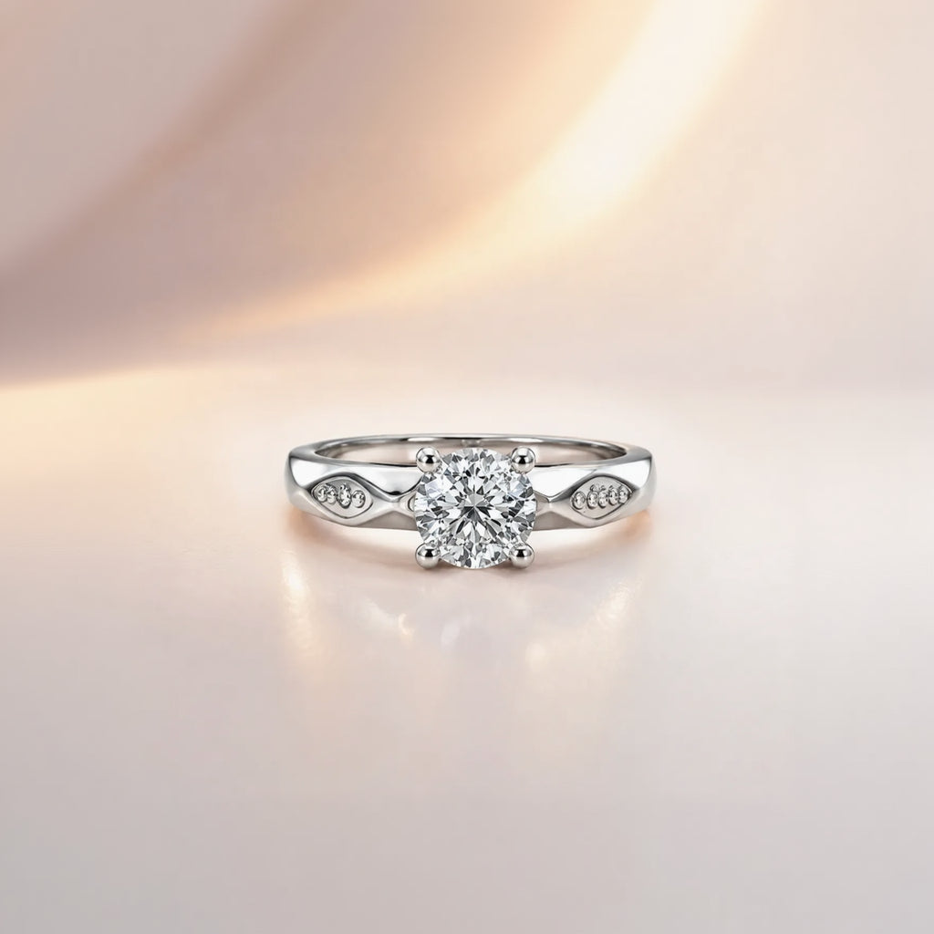 Round cut solitaire engagement ring in sterling silver with faceted shoulder detail, close-up front view on pink background